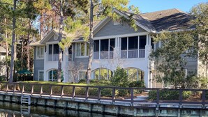 A two-story house with a balcony, a covered porch, and a reflection in the water.