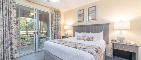 A hotel room with a large bed, two bedside lamps, a ceiling fan, and a sliding glass door leading to an outdoor area.