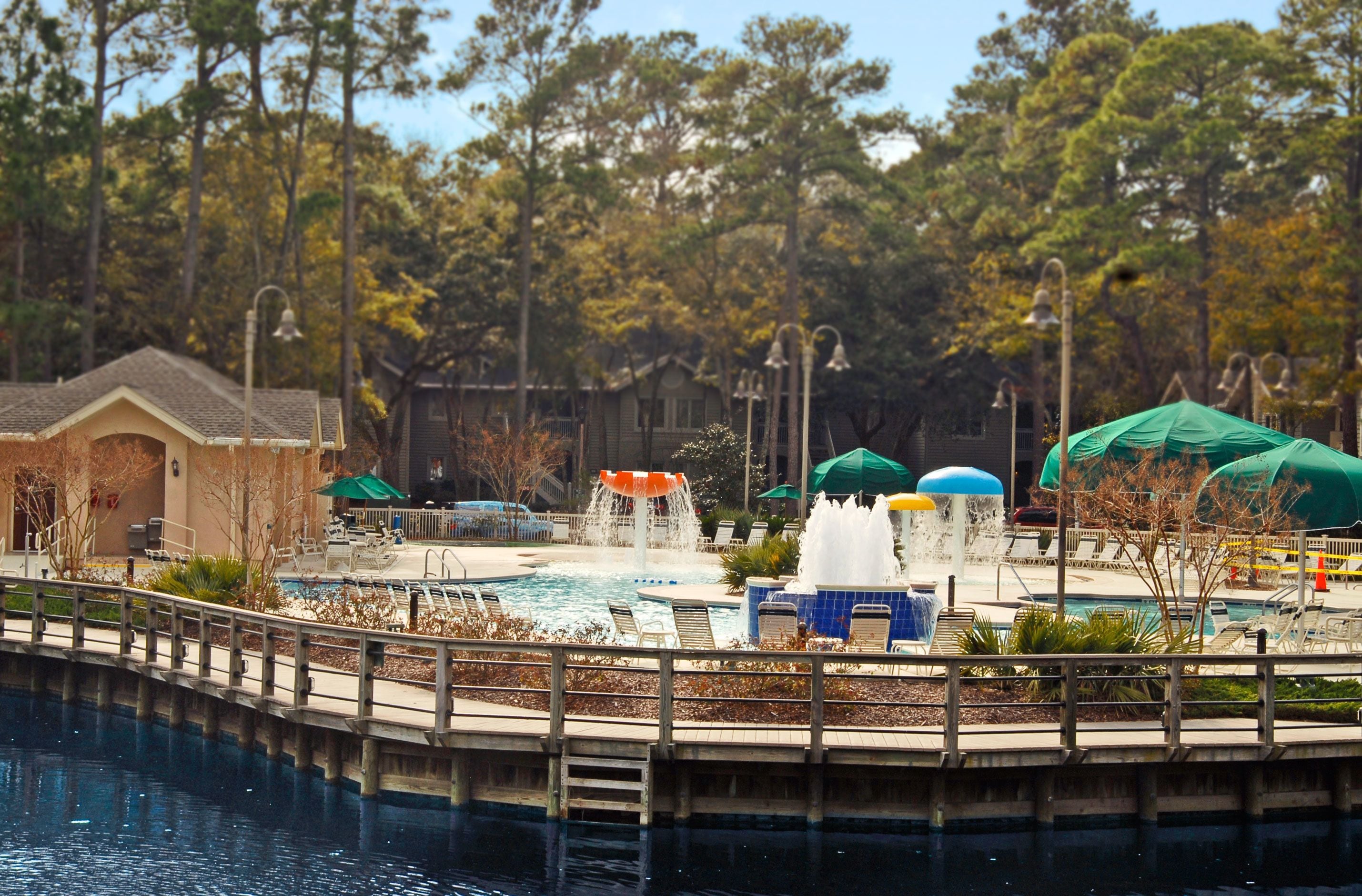 A pool area with a water fountain, lounge chairs, and umbrellas.
