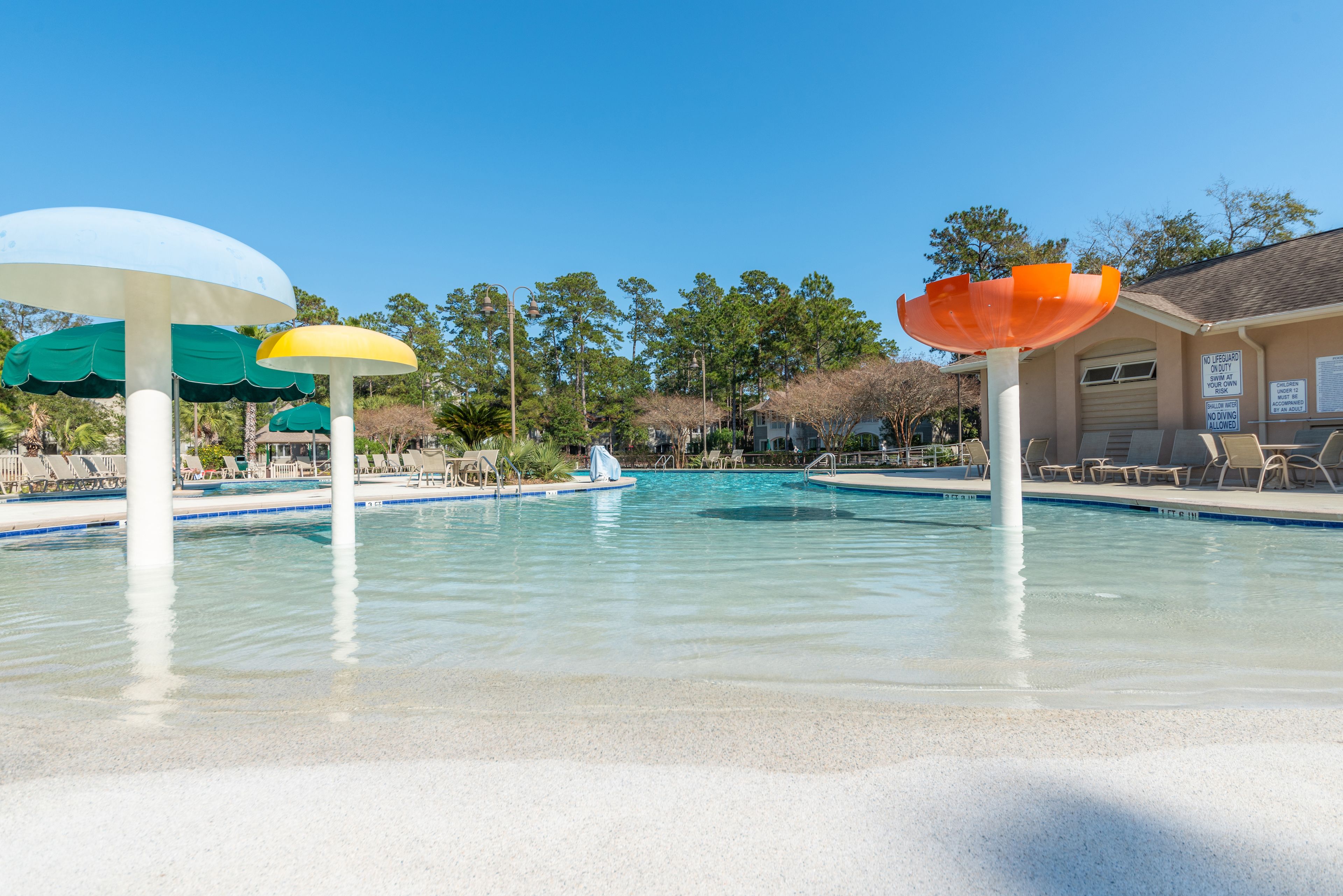 A swimming pool with colorful umbrellas, lounge chairs, and a lifeguard station.