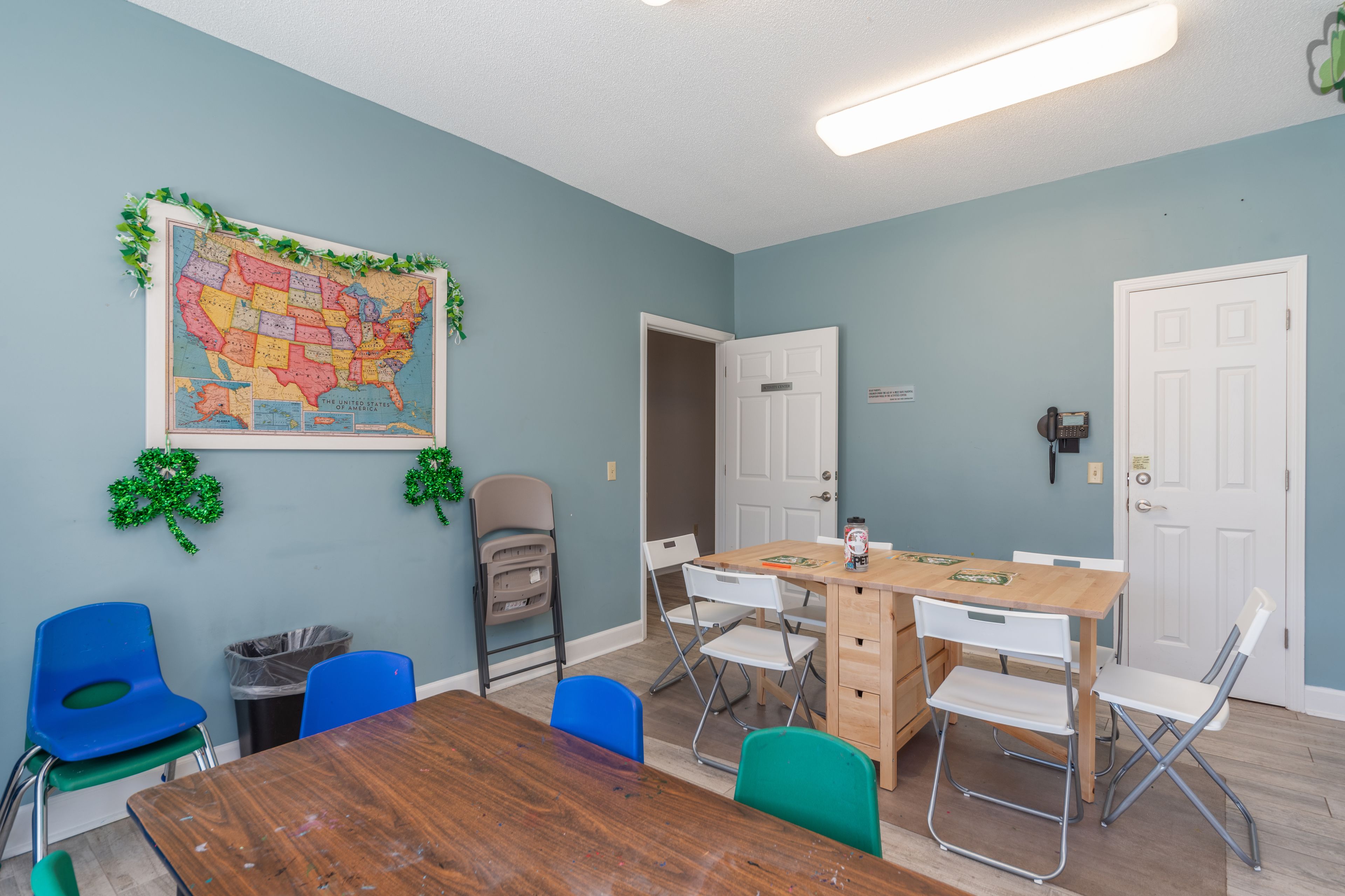 A room with a wooden table, blue and green chairs, a map on the wall, and a door.