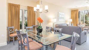 A dining area with a glass table, chairs, a chandelier, and a vase with orange flowers.