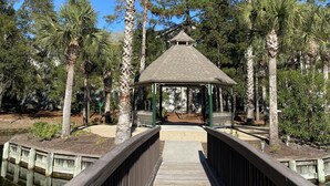 A gazebo with a wooden deck leading to it, surrounded by tall palm trees and other greenery.