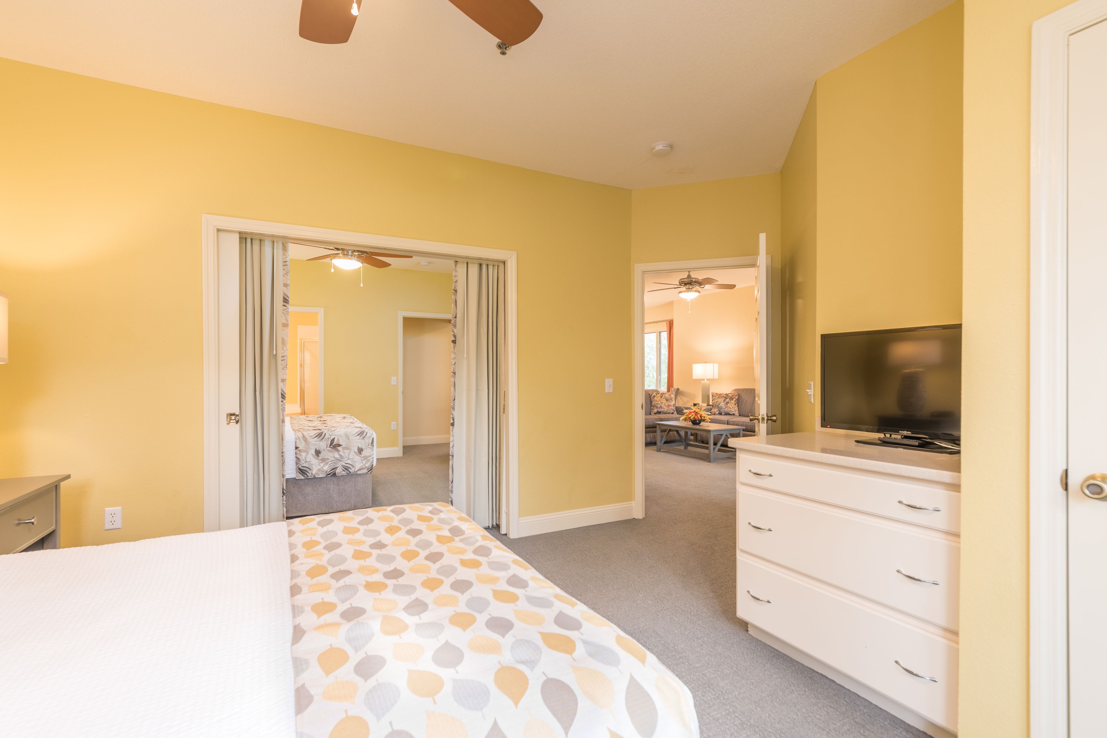 A hotel room with a bed, a dresser, a television, and a ceiling fan.