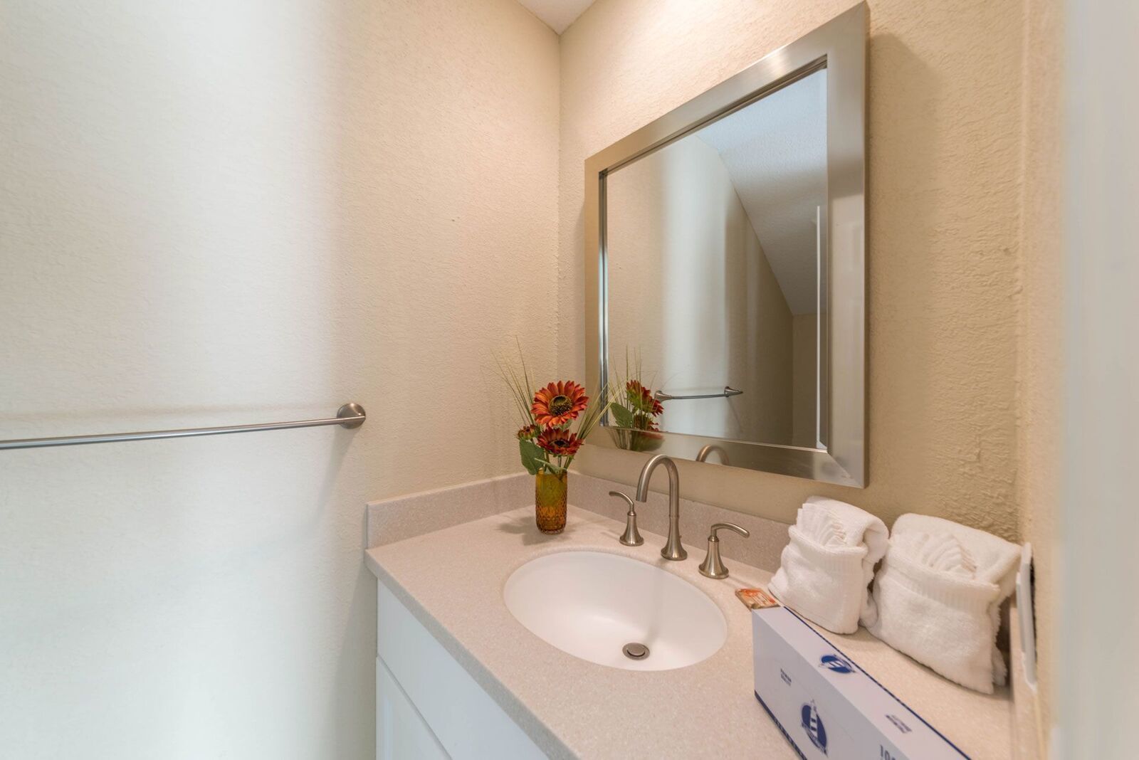 A bathroom with a white sink, two faucets, a mirror, and a towel rack with towels.