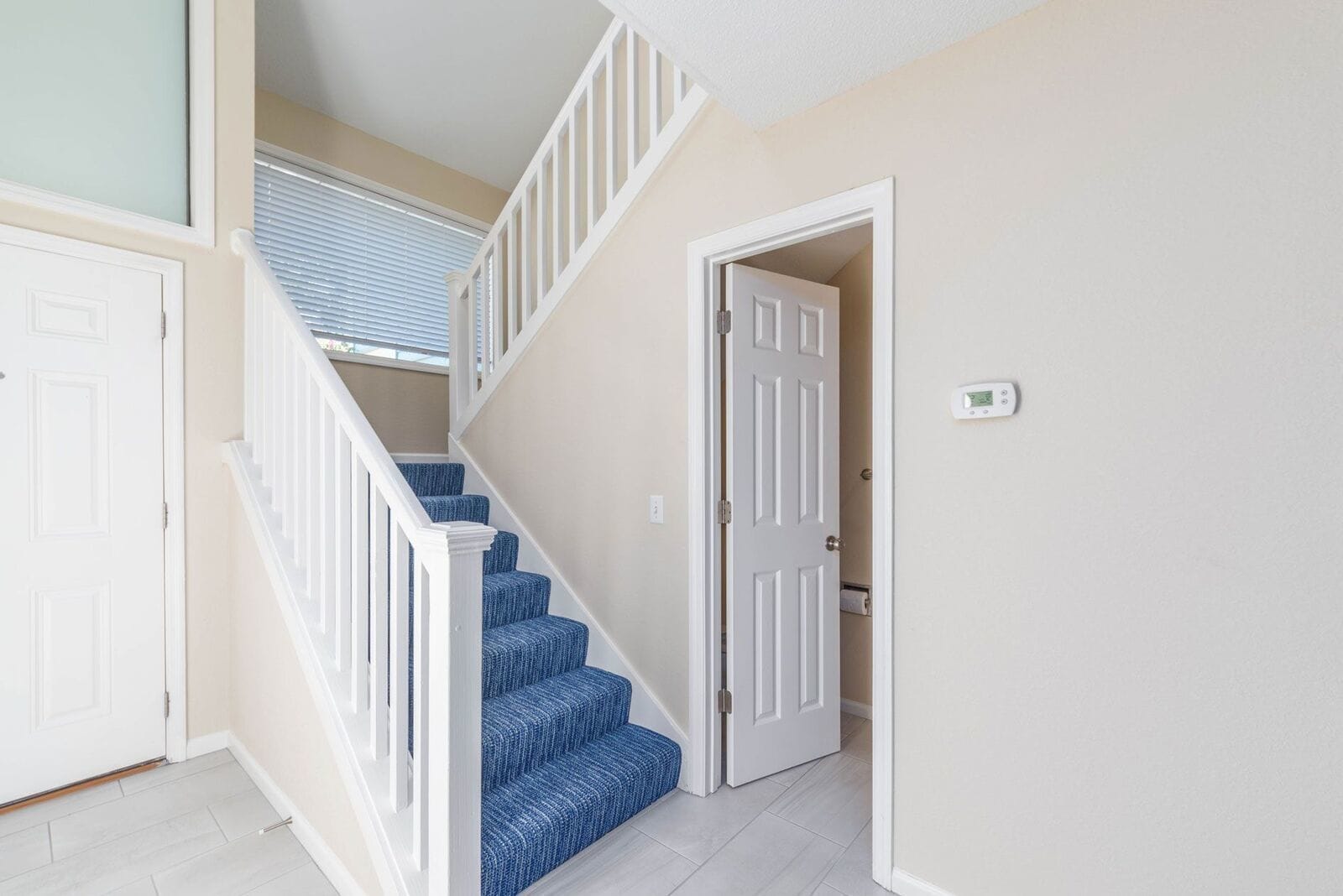 A staircase with white railings and blue carpeted steps leading to a room with beige walls and a white door.