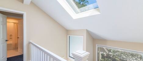A staircase with a skylight leading to a second floor, a door to a bathroom, and a window with blinds.