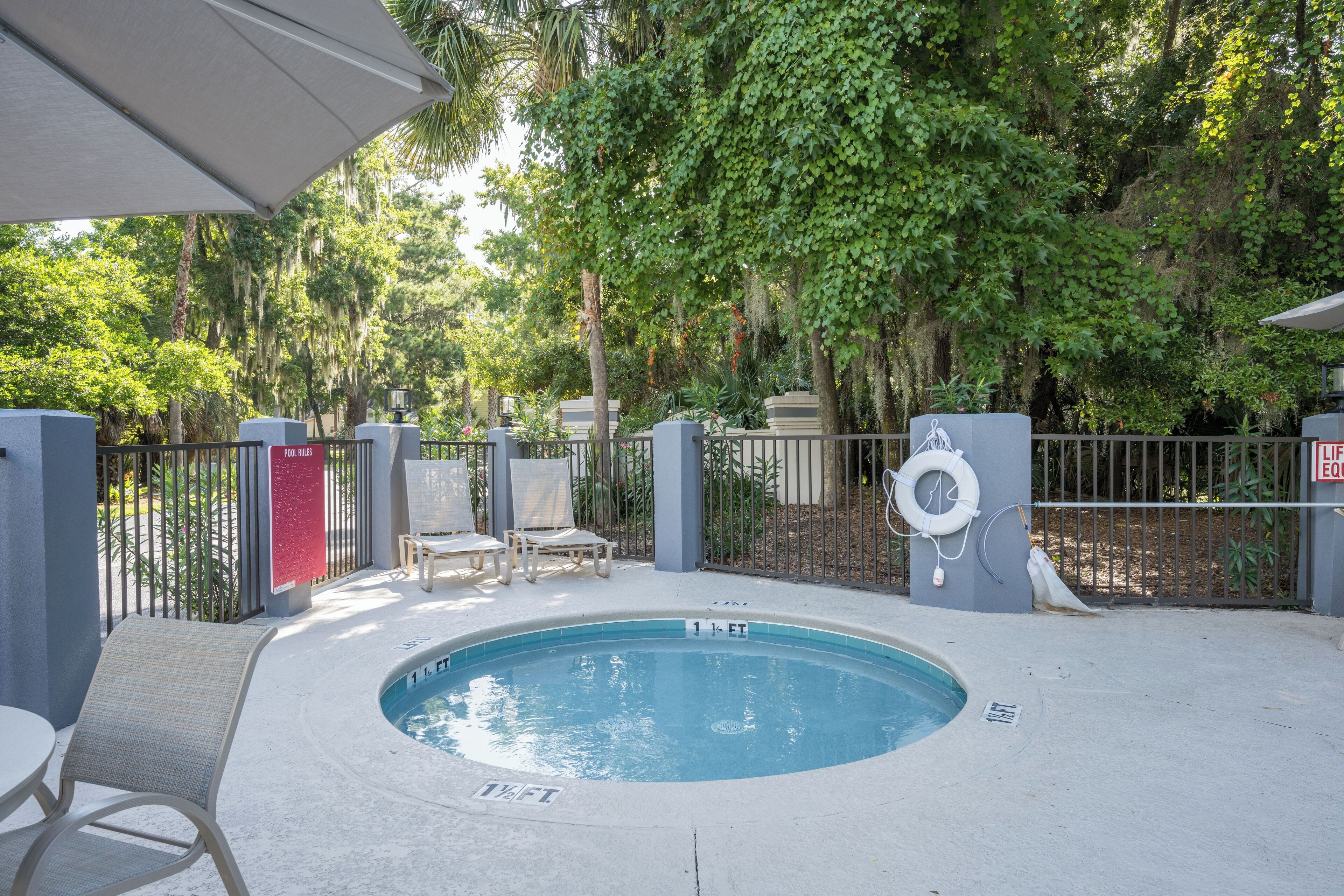 A hot tub surrounded by a pool area with lounge chairs and a fence.
