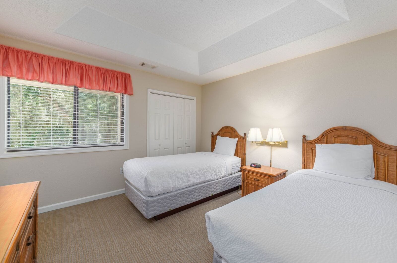 A hotel room with two beds, a nightstand with lamps, a dresser, and a window with blinds.