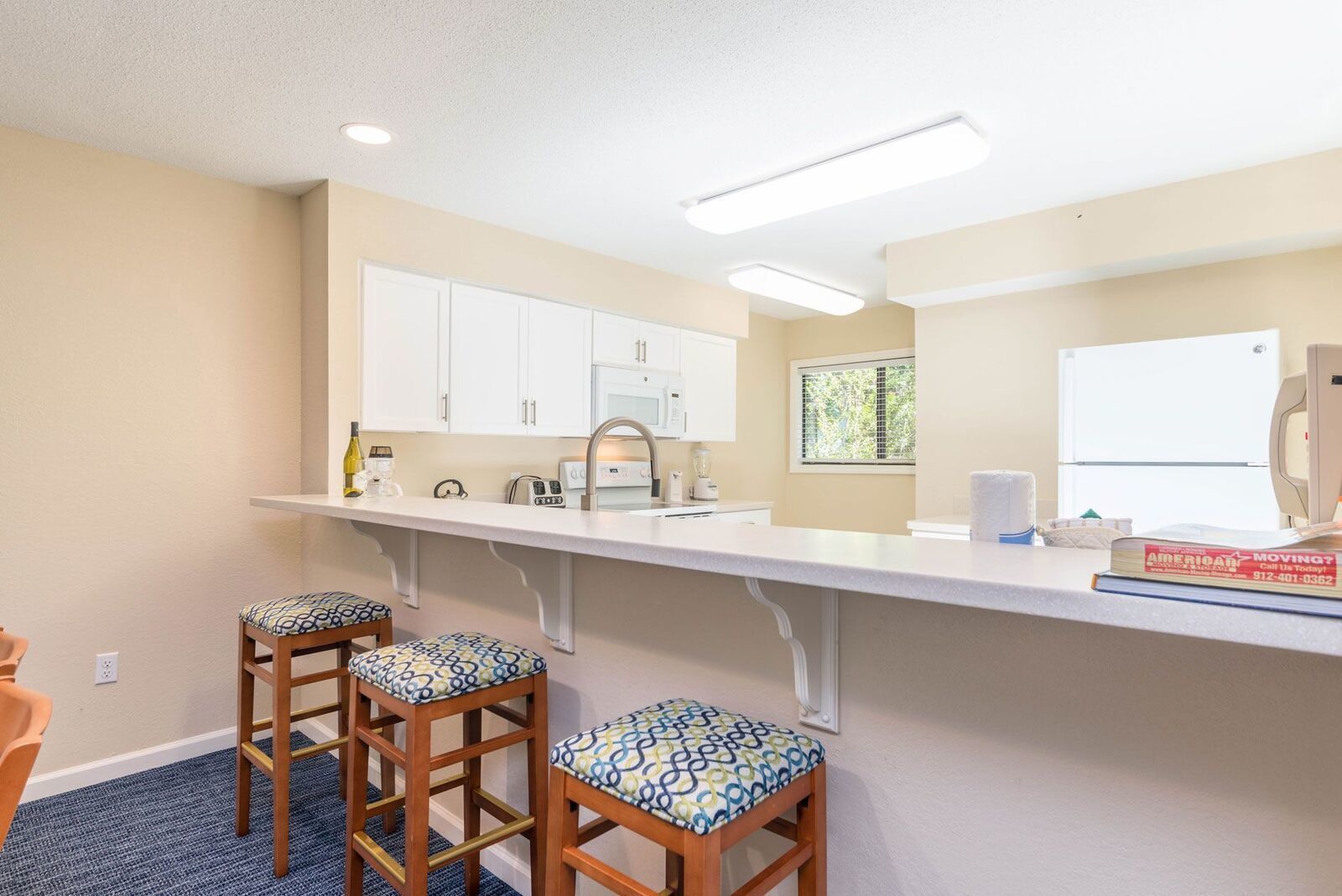 A kitchen with white cabinets, a countertop, and three stools with patterned cushions.