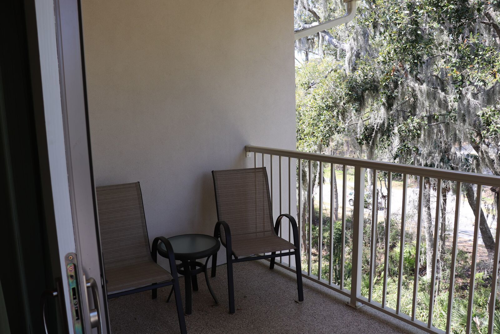 Un balcone con due sedie e un tavolino, affaccia su un paesaggio naturale con alberi e una strada.
