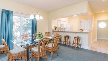 A dining area with a glass table, wicker chairs, and a kitchen in the background.