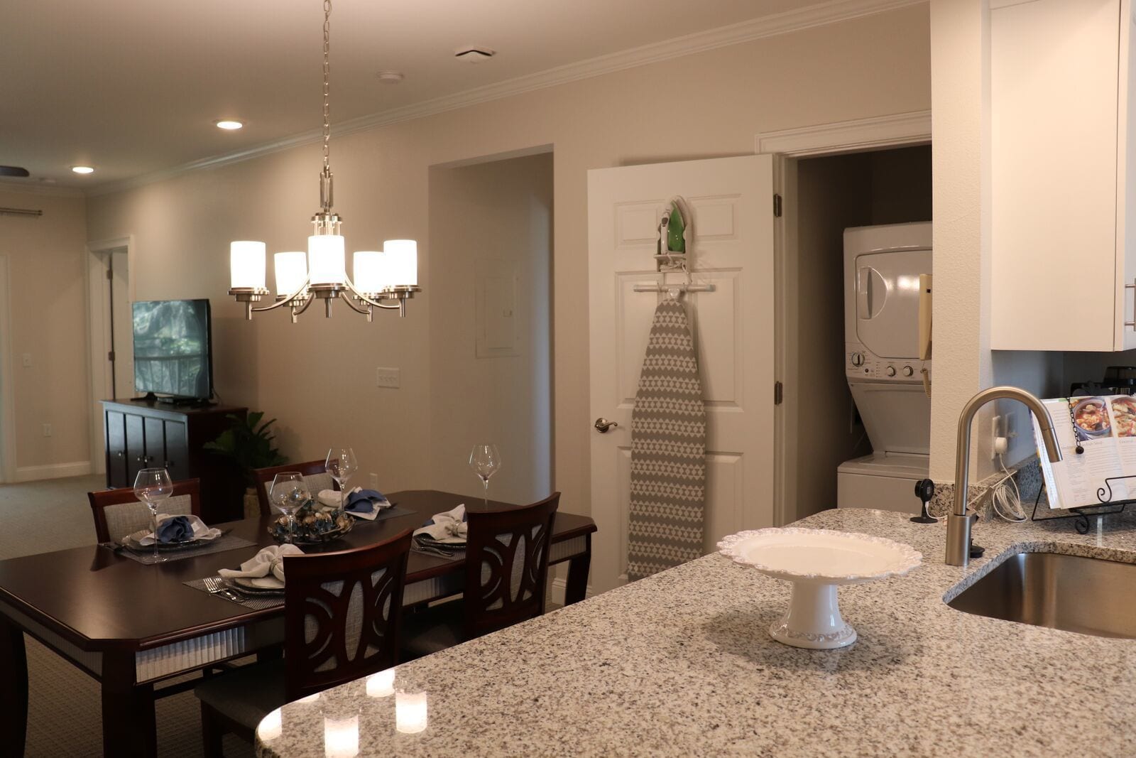 A modern kitchen with granite countertops, a built-in oven, and a dining area with a chandelier.
