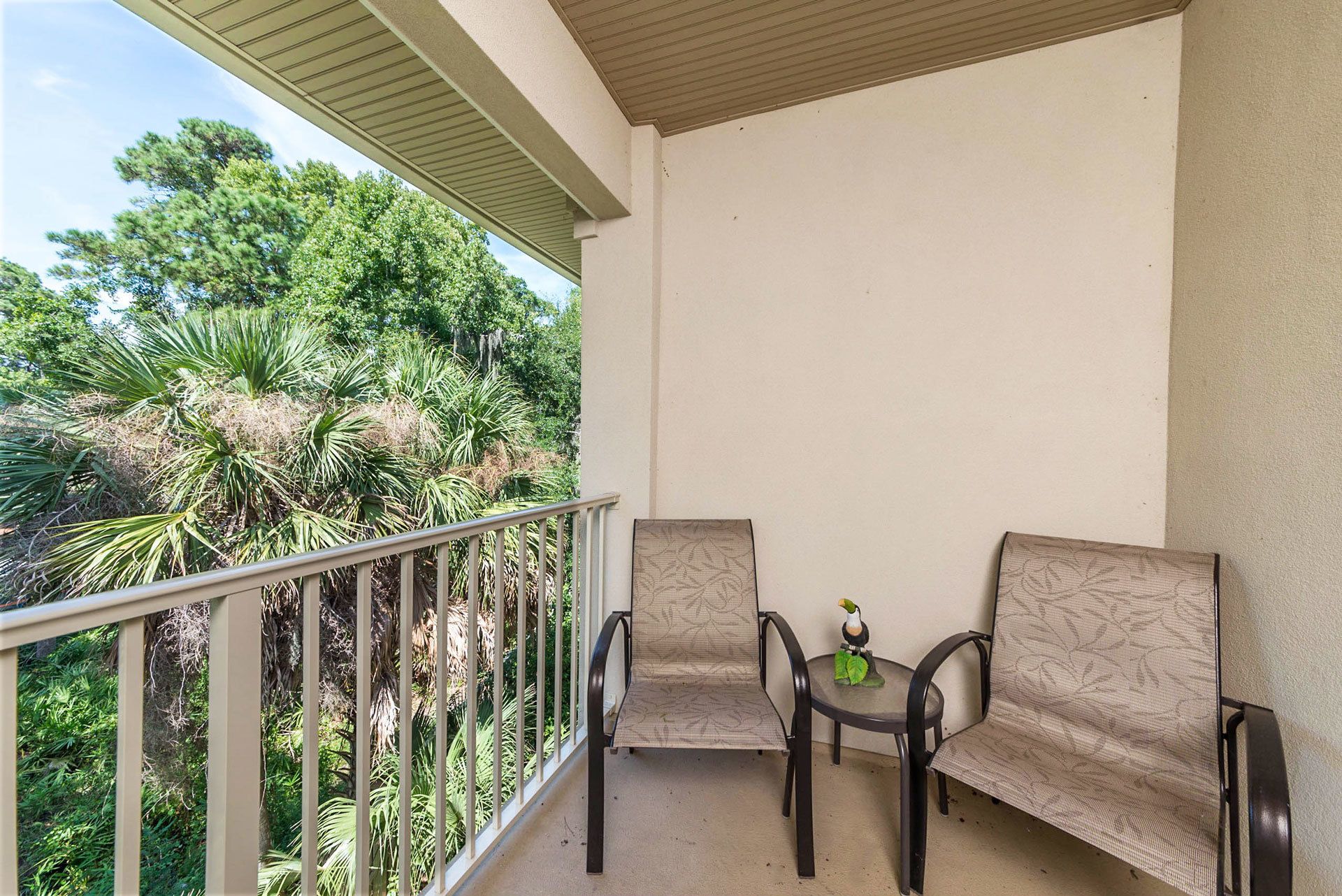 A balcony with two chairs and a small table, overlooking a lush garden with various plants and trees.