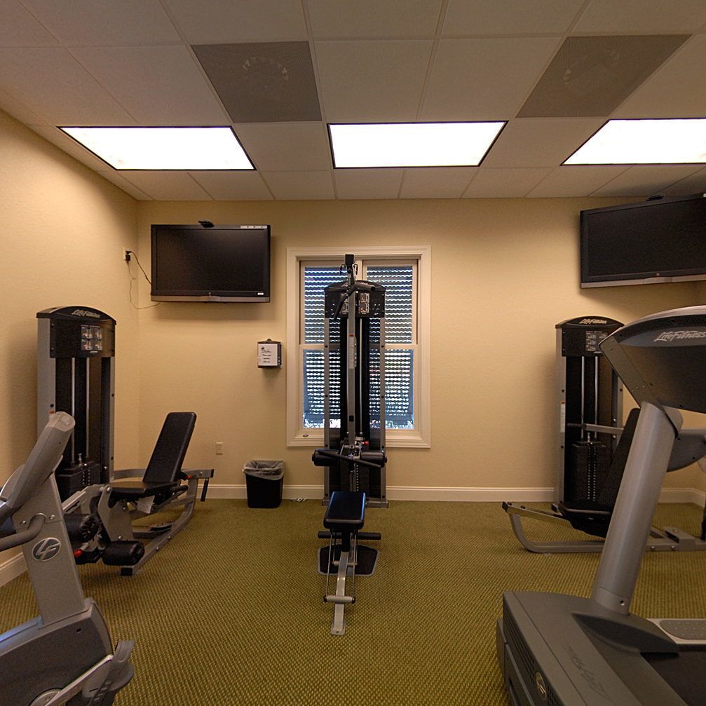 A gym with exercise equipment, a television, and a window with blinds.