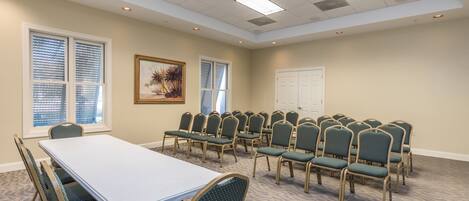 A conference room with a long table and rows of chairs, large windows, and a door.