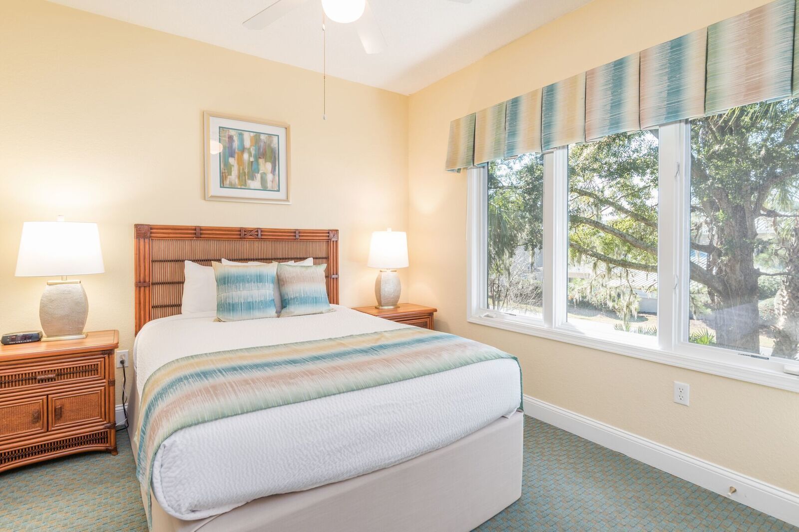 A bedroom with a bed, two bedside tables, a nightstand, a window with a view of trees, and a ceiling fan.