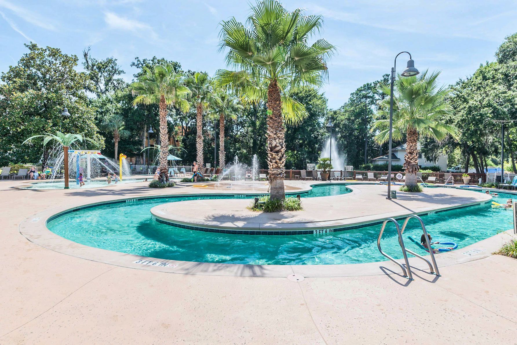 Zona de piscina con varias fuentes, palmeras y sillones de descanso.