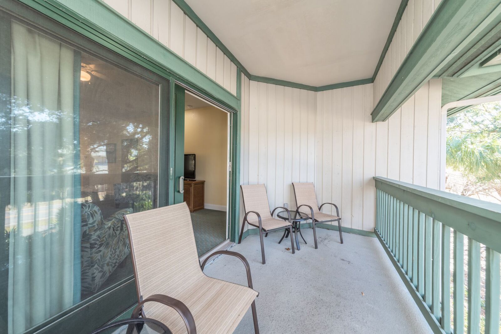 A covered porch with two chairs and a small table, a sliding glass door, and a television in the background.