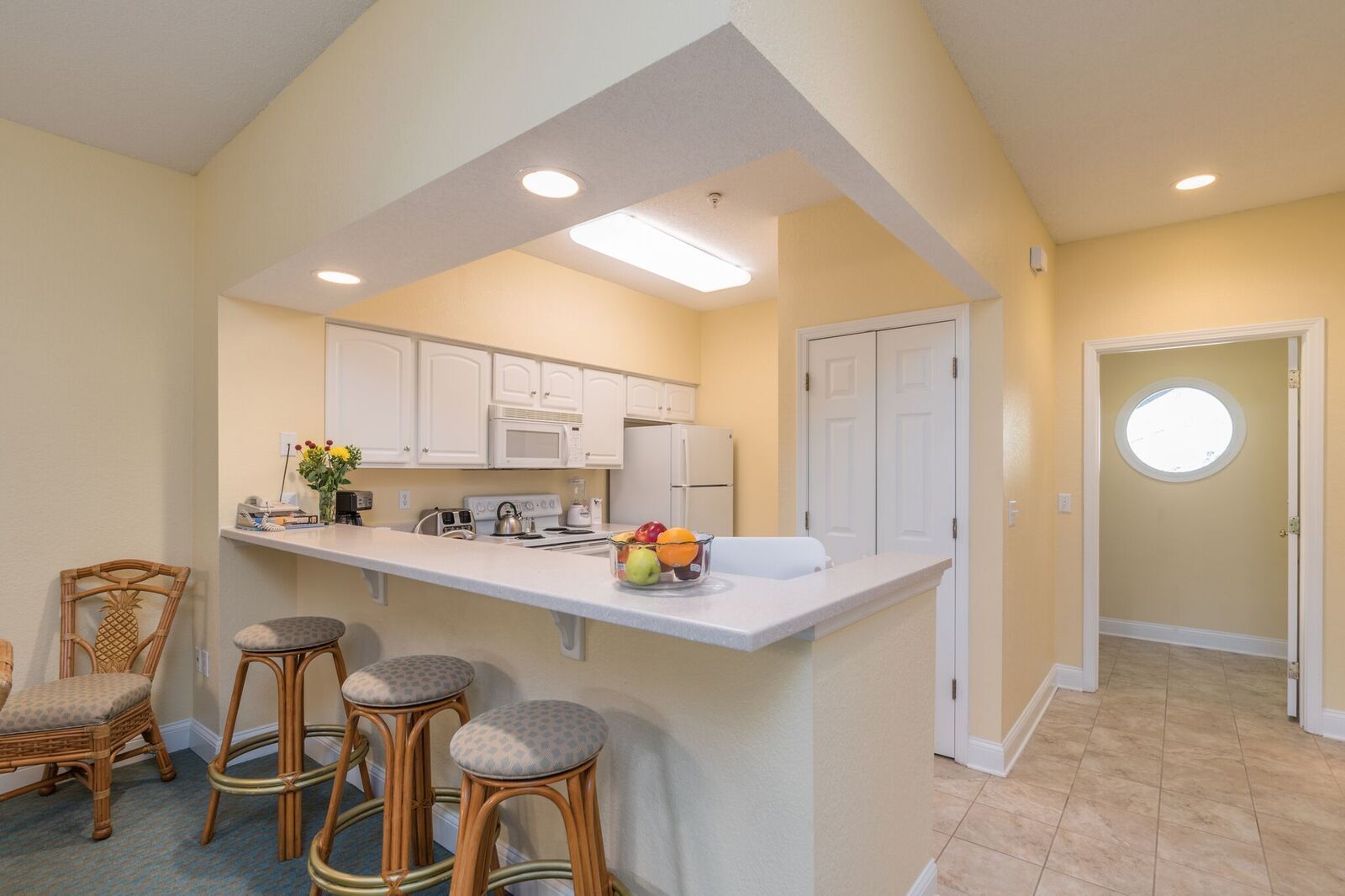 A kitchen with white cabinets, a central island with stools, a microwave, and a fruit bowl.