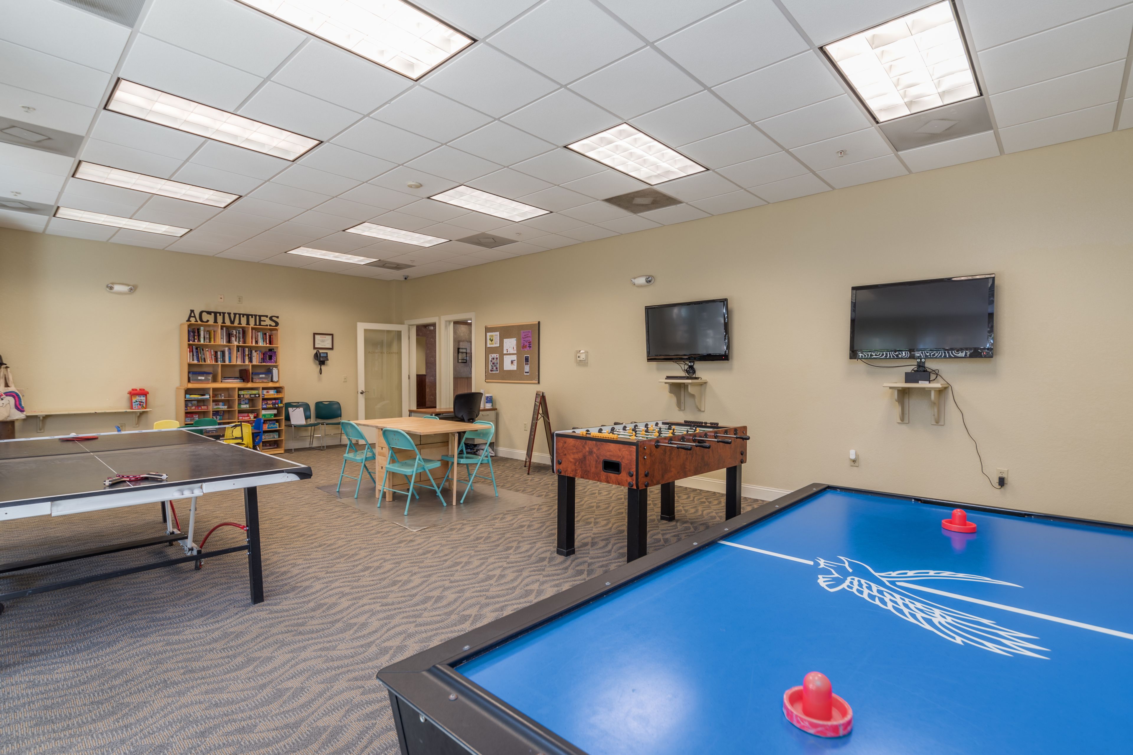 Uma sala de lazer com mesa de pebolim, mesa de ping pong e mesa de bilhar.