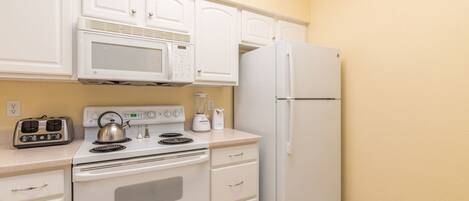 A compact kitchen with white appliances, including a microwave, stove, and refrigerator, and a toaster on the countertop.