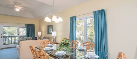 A dining area with a glass table, wicker chairs, and a sofa in the background.