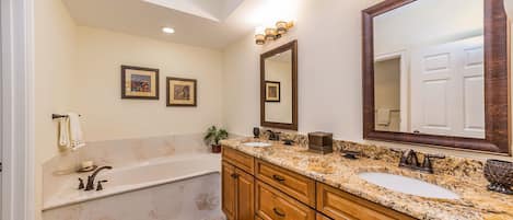 Une salle de bain avec une baignoire, un lavabo et un grand miroir. On y trouve des meubles en bois et un comptoir en marbre.