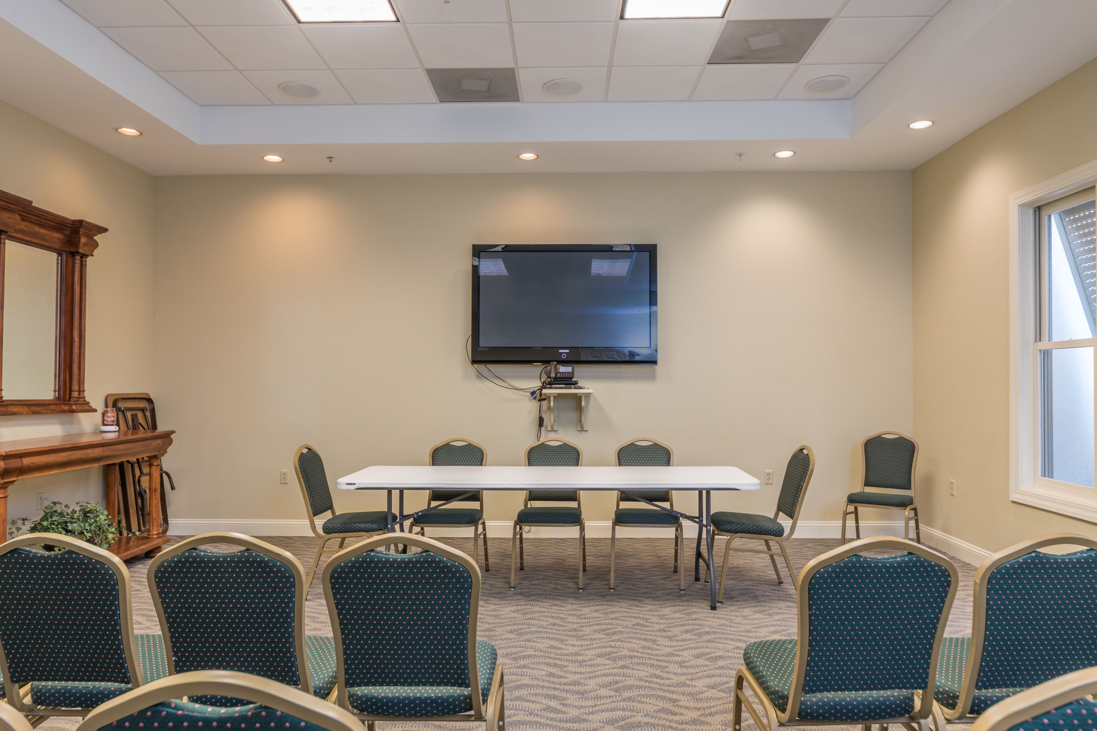 A conference room with a large table, six chairs, a flat-screen TV, and a window.