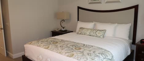 A neatly made bed with a floral bedspread, a bedside lamp, and two framed floral paintings on the wall.