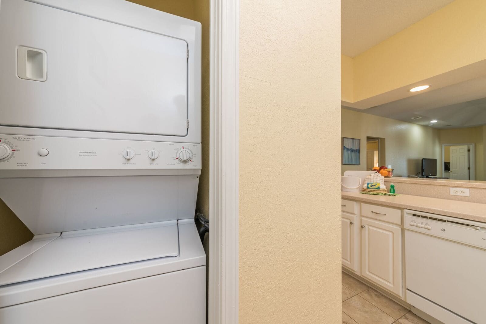 A laundry area with stacked washers and dryers, a kitchen with white cabinets, and a beige wall.