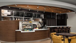 A modern bistro bar with a curved wooden counter, a menu board, and yellow chairs around a table. - Residence Inn by Marriott Syracuse Downtown at Armory Square (Syracuse)