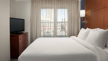 A hotel room with a large bed, a TV on a wooden dresser, and a view of buildings through sheer curtains.