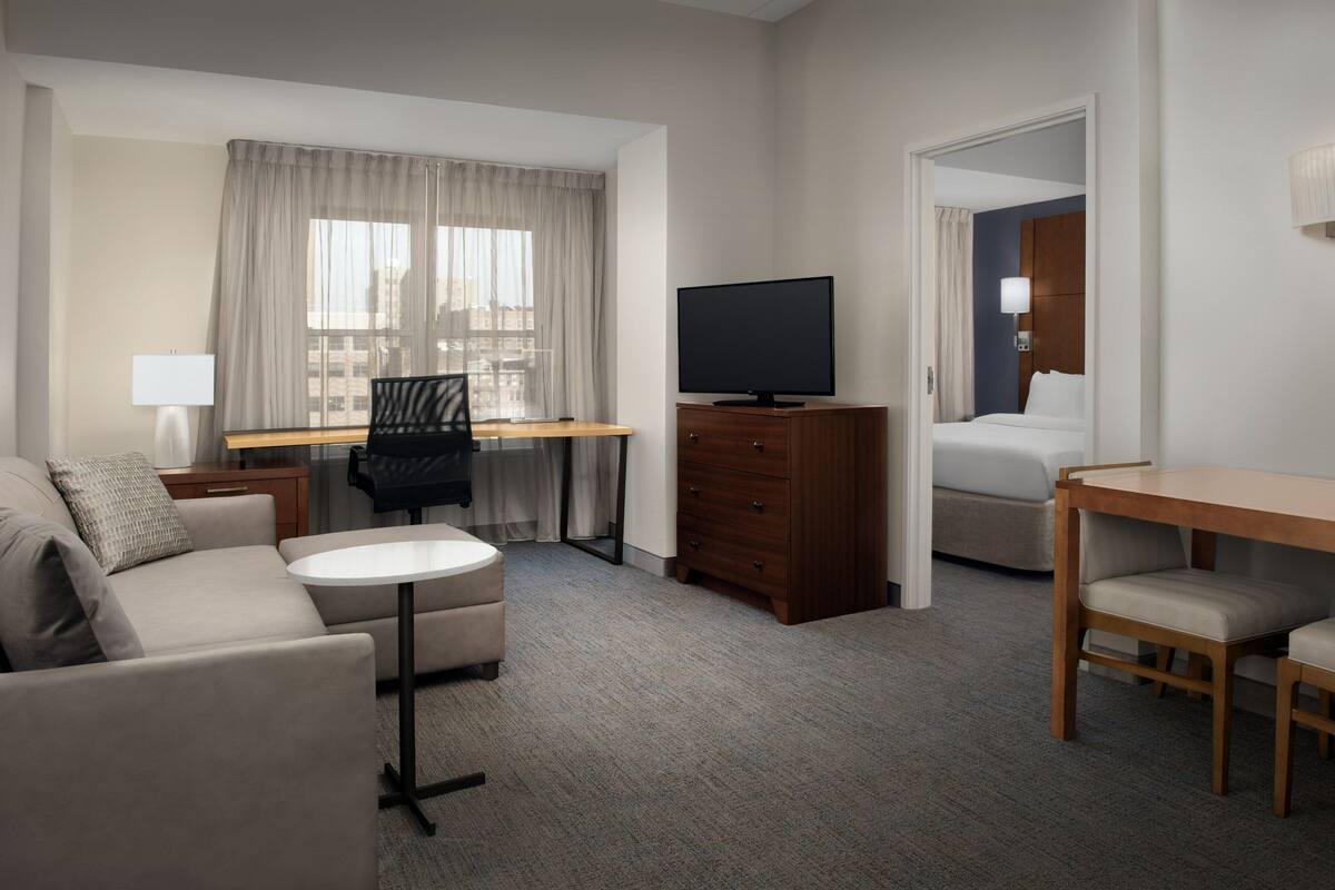 A hotel room with a sofa, a desk with a chair, a television, a bed, and a small table.