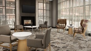A modern lounge area with leather chairs, a fireplace, and large windows offering city views. - Residence Inn by Marriott Syracuse Downtown at Armory Square (Syracuse)