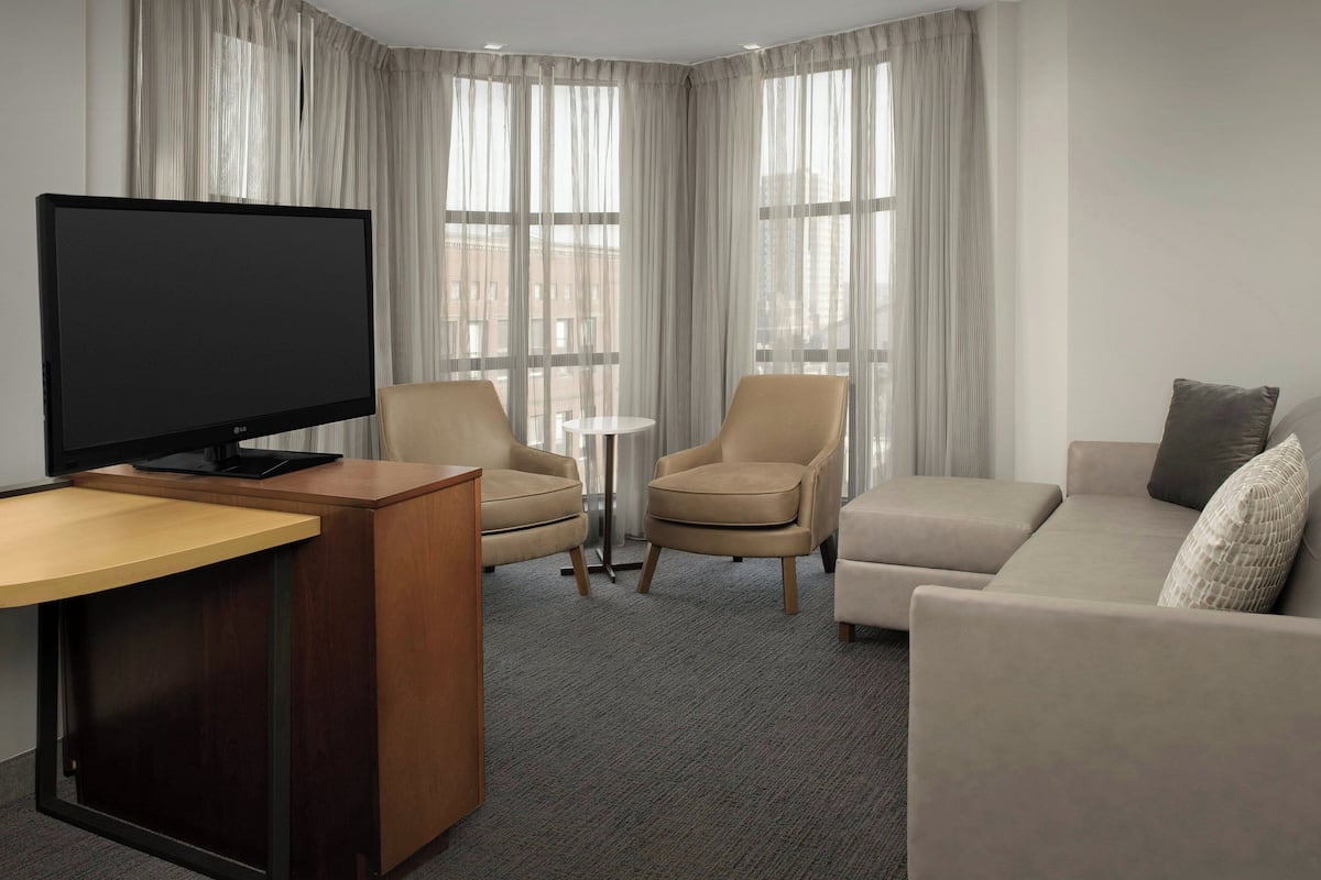 A modern hotel room with a flat-screen TV, two armchairs, a sofa, and a small round table.
