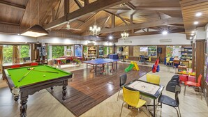 Een ruime binnenspeelruimte met een pooltafel, tafeltennistafel en diverse speelattributen voor kinderen.