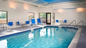 Een binnenzwembad met helderblauw water, omringd door blauwe stoelen en tafels, en voorzien van een zwemtrap.