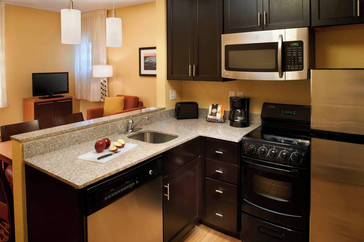 Cocina compacta con microondas, estufa y lavavajillas. Cuenta con un pequeño comedor con mesa y sillas.
