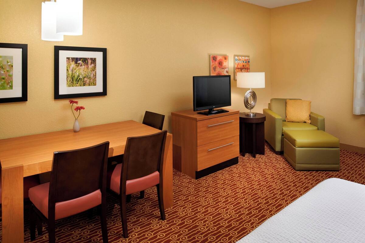 Habitación de hotel con escritorio de madera, dos sillas, televisor, lámpara, sofá y cama.