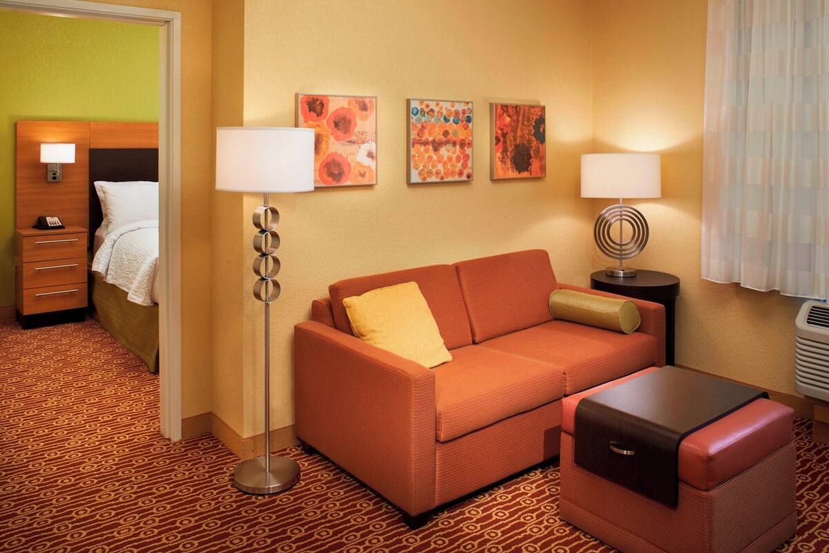 Habitación de hotel con sofá, una mesita, lámpara, cama y obras de arte en la pared.
