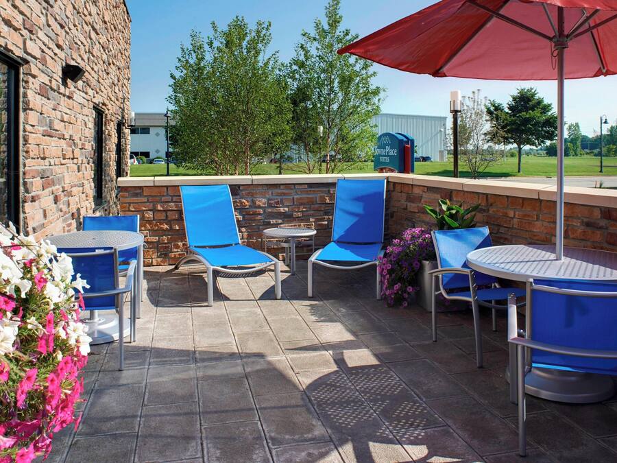 An outdoor patio with blue chairs and a red umbrella, brick walls, and a view of a building in the background.