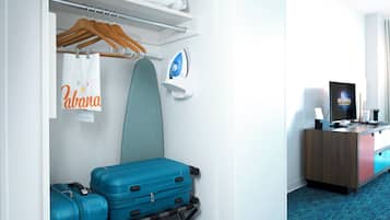 Quarto de hotel com uma cama, uma escrivaninha com computador, uma televisão, um centro de engomar na parede e um porta-bagagem.