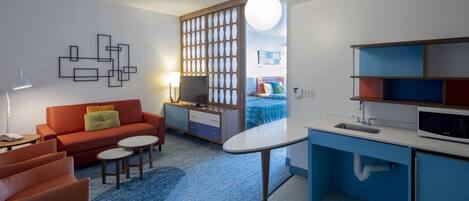A modern living room with a sofa, coffee table, and a kitchen area with a sink and microwave.