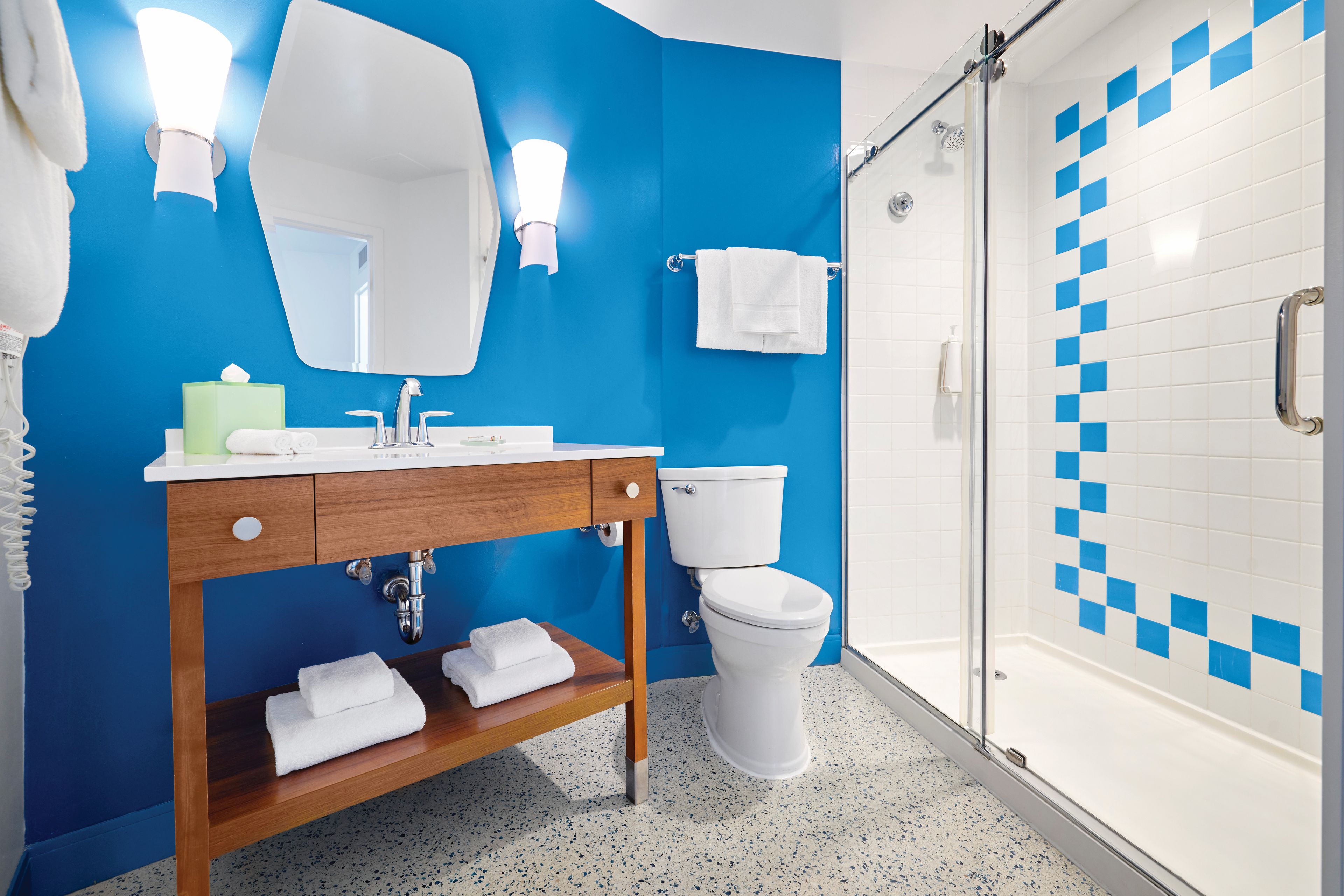Un baño con pared azul, lavamanos blanco, inodoro y zona de ducha.