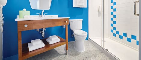 Un baño con pared azul, lavamanos blanco, inodoro y zona de ducha.