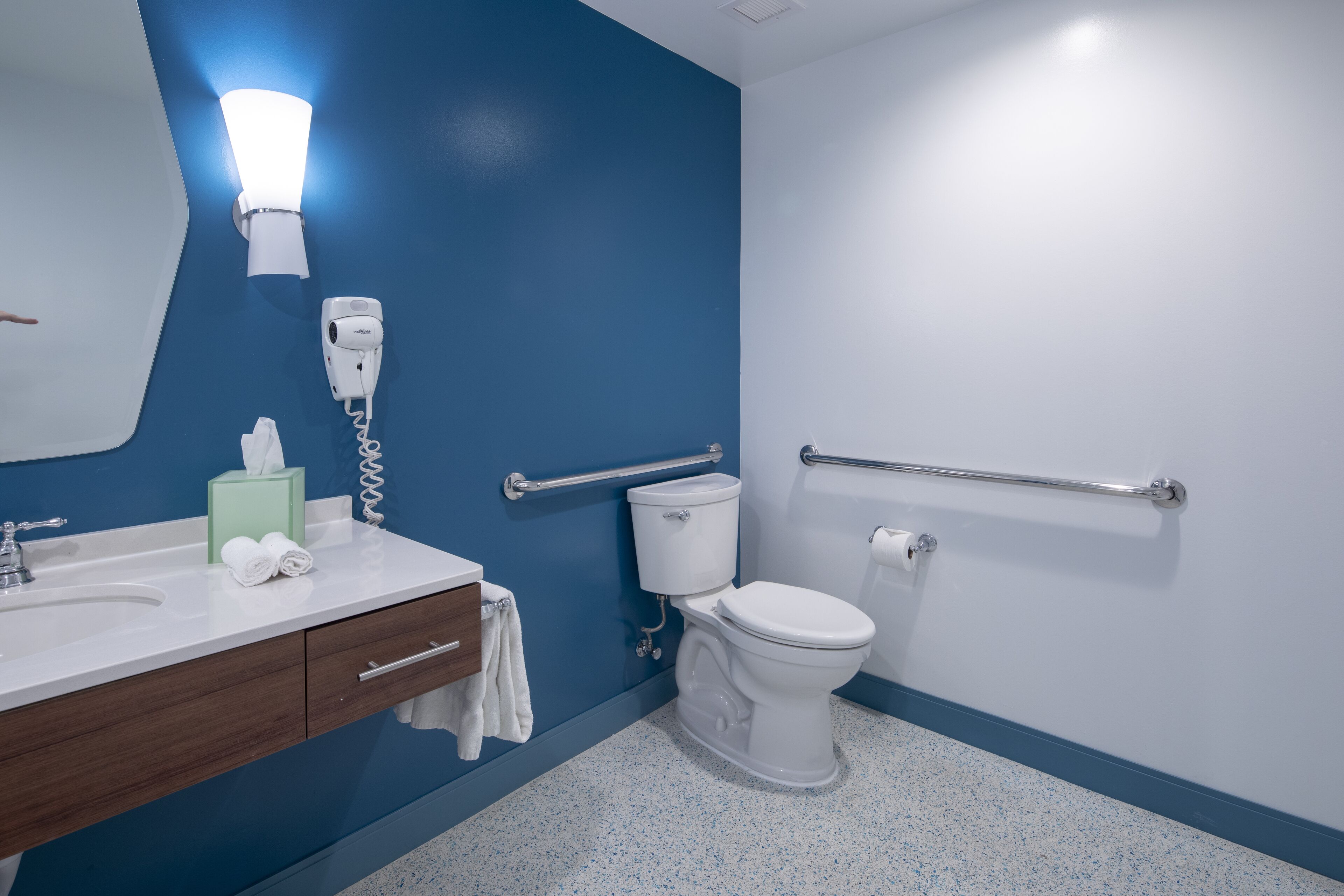 Une salle de bain avec un mur bleu, des toilettes blanches et un lavabo avec un miroir.