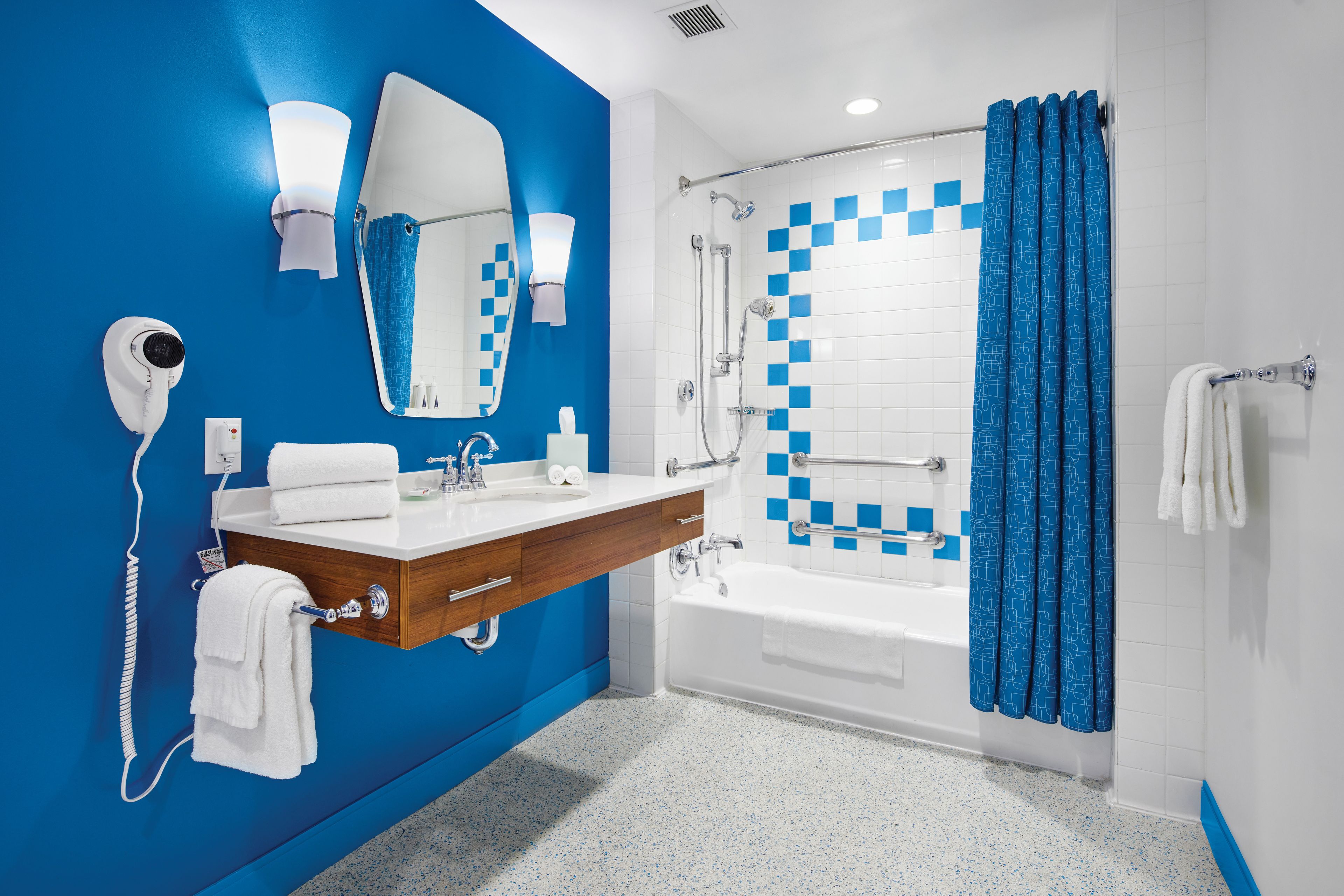 A bathroom with a blue wall, white tiles, a bathtub, a shower, a vanity with a mirror, and a towel rack.