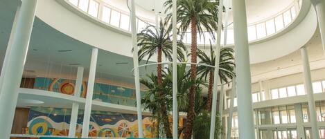 Un amplio atrium con techos altos, ventanas grandes y una columna central con palmeras.