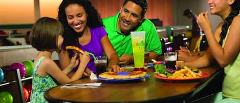 Una familia cenando en un restaurante de bolera, con comida y bebidas sobre la mesa.